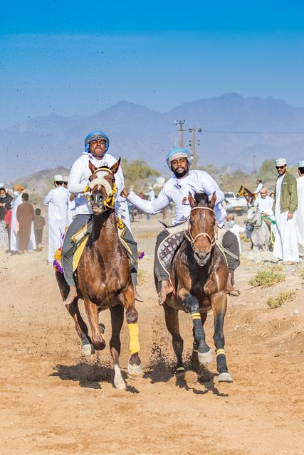 Two riders racing side by side with mountains behind