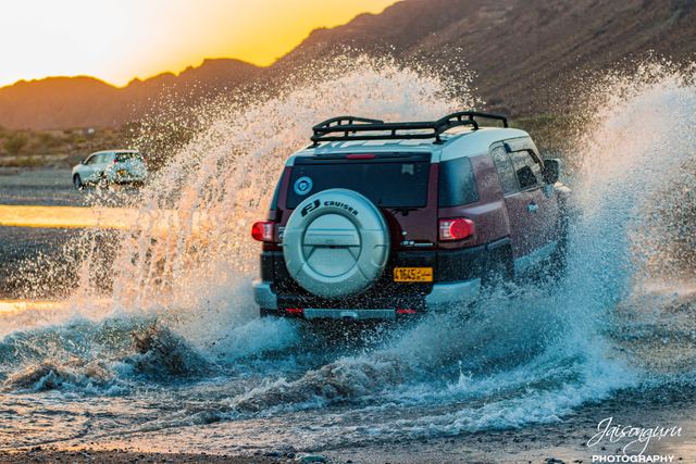 Four-wheel drive ploughing through a wave of spray at sunset