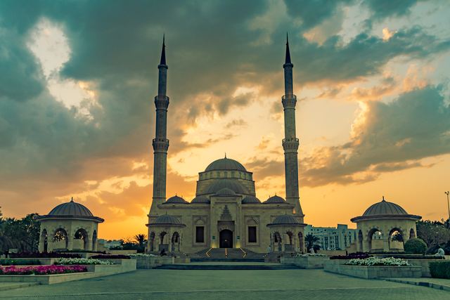 Mosque in silhouette against a gold and teal sunset sky