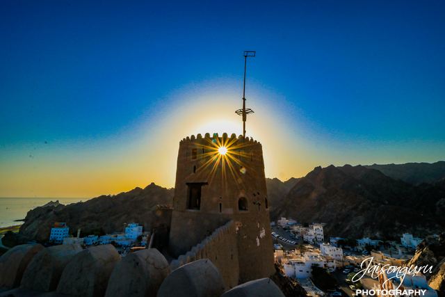 Sunburst breaking over a restored watchtower above a village