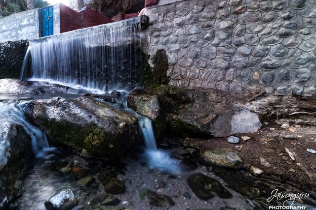Falaj water spilling over a stone wall into the wadi