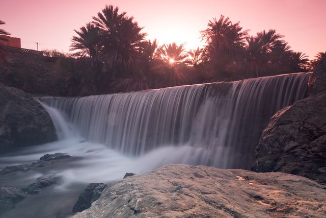 Waterfall at sunset with date palms along the ridge