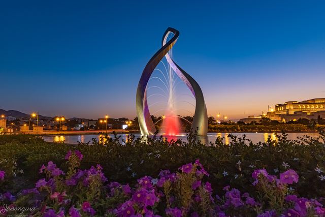 Sculpture lit at dusk above a bed of flowering bougainvillea