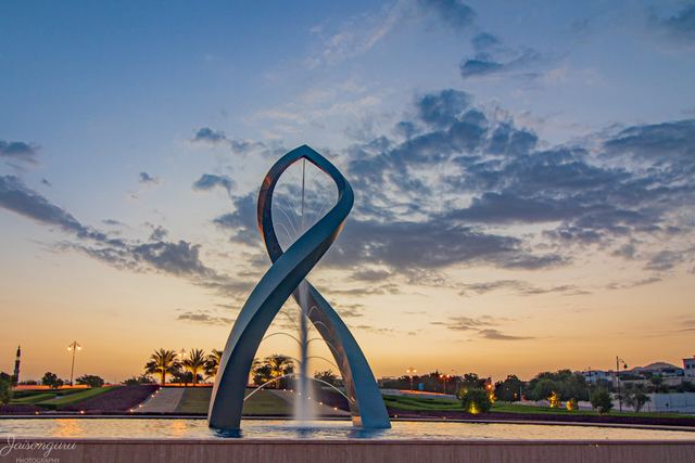Sail-shaped sculpture and fountain against an evening sky