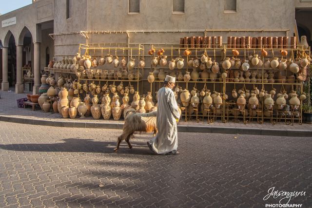 Lone figure walking past rows of clay pots stacked outside the souq
