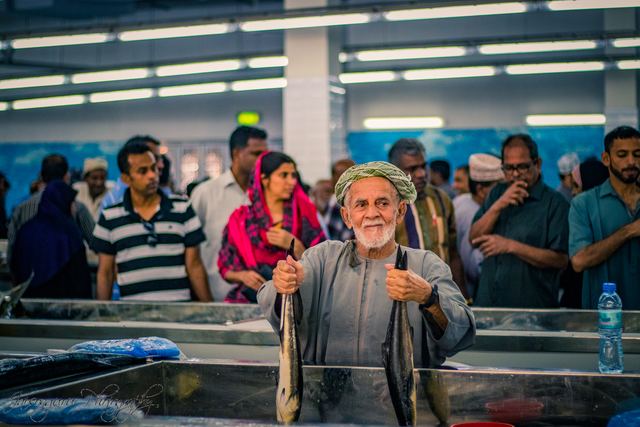 Elderly man holding a fish above the counter in a busy fish market
