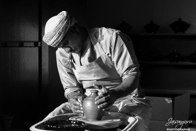 Black and white frame of a potter shaping clay on the wheel