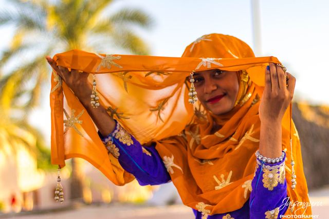 Woman in an orange veil turning to the camera in the sunlight