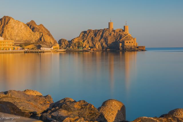 Golden early light on a fort above the bay, boulders in the foreground