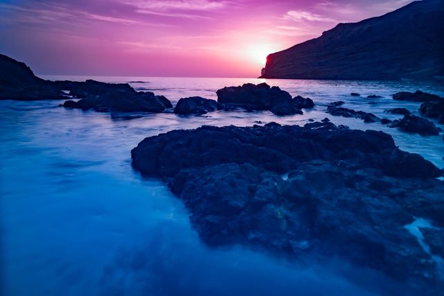 Long exposure at blue hour, magenta sky above rocks and smooth water
