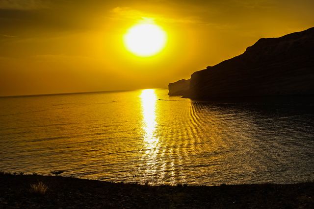 Low sun burning through haze above a headland, light spilling across the sea