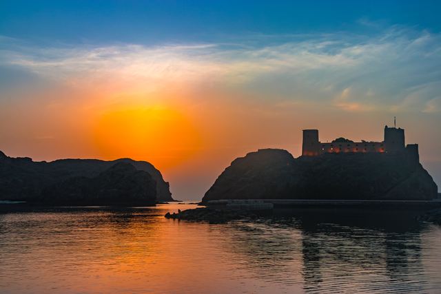 Sunrise behind a fort on a rocky island, calm water in the foreground